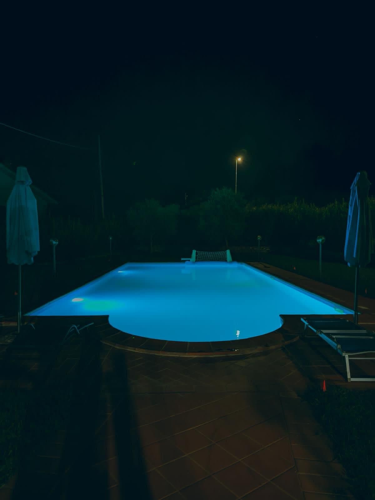 The pool lit at night with loungers and parasols